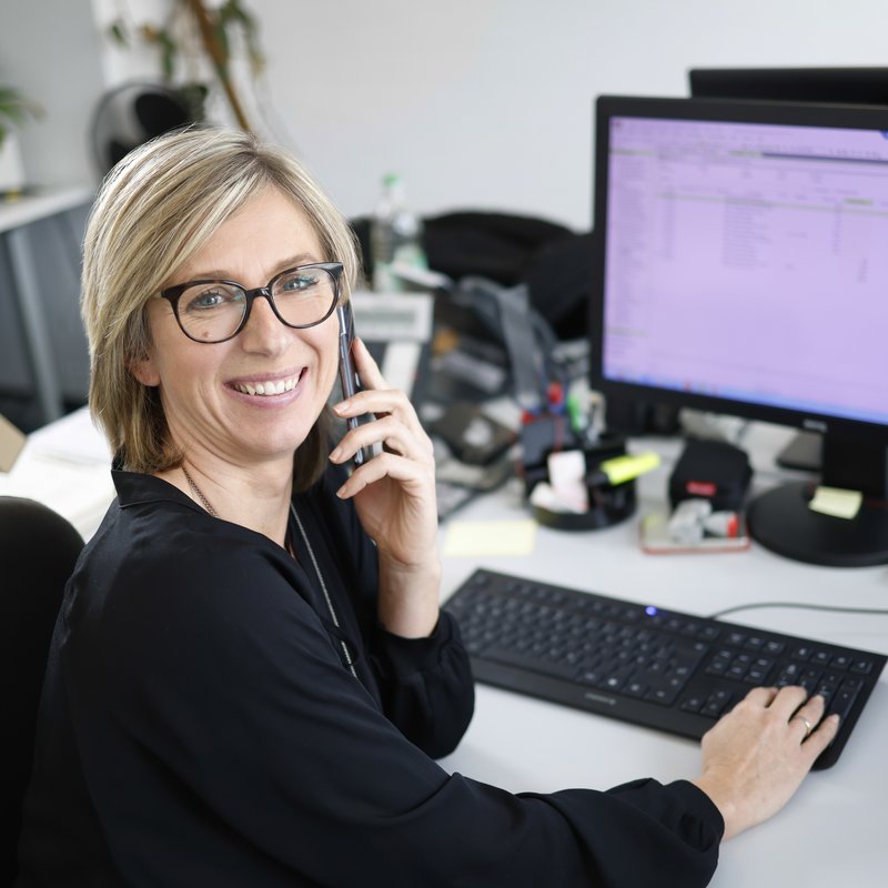 Mitarbeiterin mit Telefon am Ohr vor Bildschirm